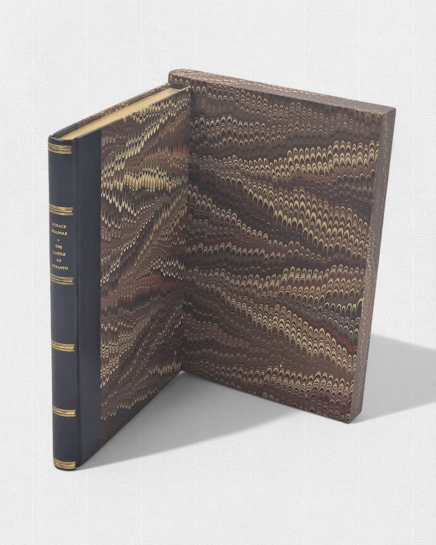 A luxurious 2022 Rambler Press edition of The Castle of Otranto by Horace Walpole, limited to 25 hand-numbered copies. The octavo book, printed on Century Laid cotton paper with watermarks in Monotype Bell typeface, features a half-leather binding with hand-marbled paper sides, gilded edges, and a custom slipcase. The cover evokes the eerie Gothic atmosphere of the 1764 novel, with shadowy castle motifs and intricate detailing, reflecting its status as the cornerstone of the Gothic genre.