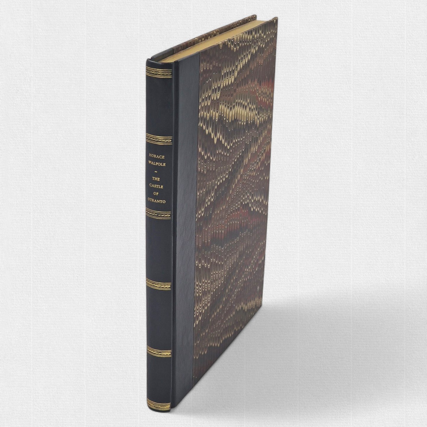 A luxurious 2022 Rambler Press edition of The Castle of Otranto by Horace Walpole, limited to 25 hand-numbered copies. The octavo book, printed on Century Laid cotton paper with watermarks in Monotype Bell typeface, features a half-leather binding with hand-marbled paper sides, gilded edges, and a custom slipcase. The cover evokes the eerie Gothic atmosphere of the 1764 novel, with shadowy castle motifs and intricate detailing, reflecting its status as the cornerstone of the Gothic genre.